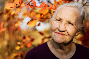 Close of senior woman under a beautiful tree with Autumn colored leaves